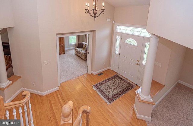 entryway with visible vents, baseboards, ornate columns, an inviting chandelier, and light wood-style floors