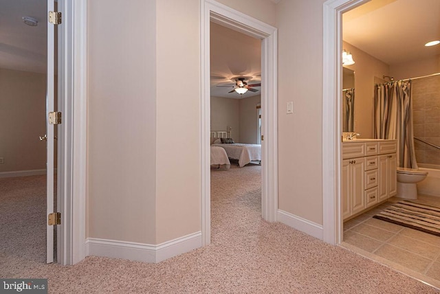 corridor with light carpet, a sink, and baseboards