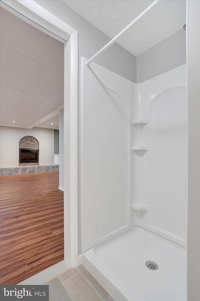 bathroom with wood finished floors, a fireplace with raised hearth, and a shower stall