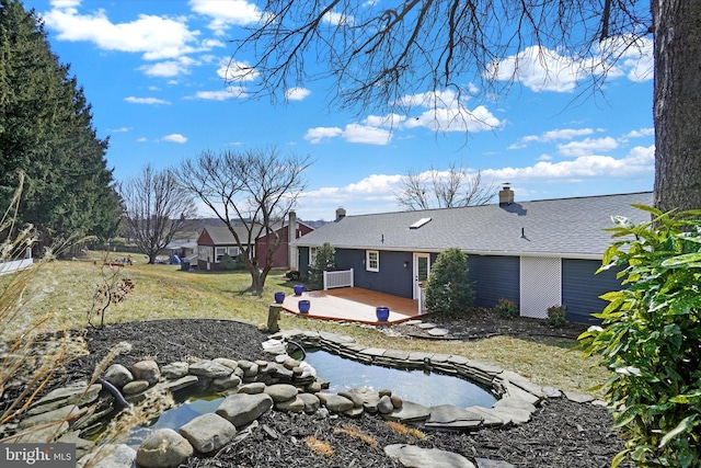 rear view of property featuring a wooden deck, a lawn, roof with shingles, and a chimney