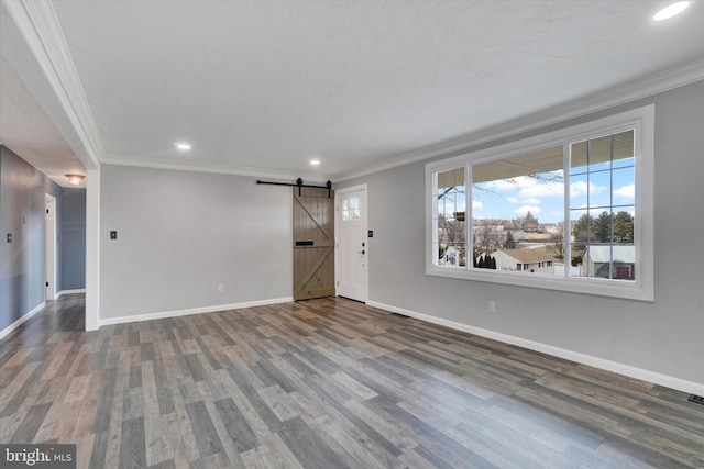 unfurnished living room with a barn door, baseboards, wood finished floors, and crown molding