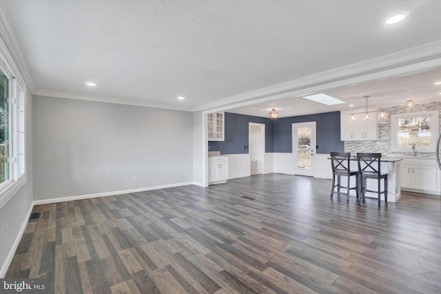 unfurnished living room featuring dark wood finished floors, crown molding, baseboards, and a sink