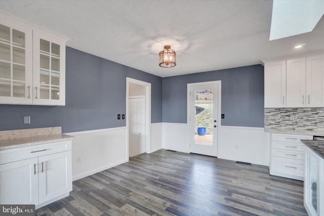 kitchen with white cabinetry, dark wood-style floors, glass insert cabinets, and wainscoting