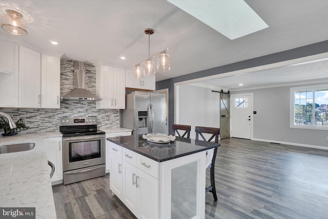 kitchen featuring a sink, backsplash, stainless steel appliances, a barn door, and wall chimney exhaust hood