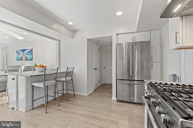 kitchen with wall chimney exhaust hood, appliances with stainless steel finishes, a breakfast bar, light stone countertops, and white cabinetry