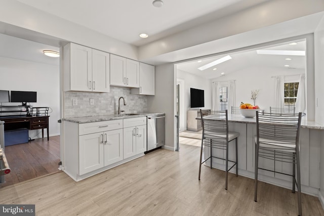 kitchen with light stone counters, light wood finished floors, white cabinetry, a sink, and dishwasher