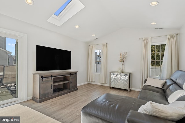 living room featuring a wealth of natural light, vaulted ceiling with skylight, visible vents, and wood finished floors