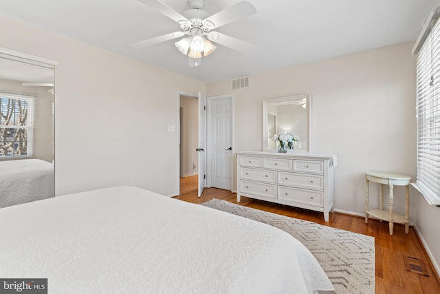 bedroom featuring a ceiling fan, visible vents, baseboards, and wood finished floors