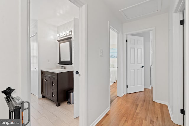 hall featuring baseboards, a sink, attic access, and light wood-style floors