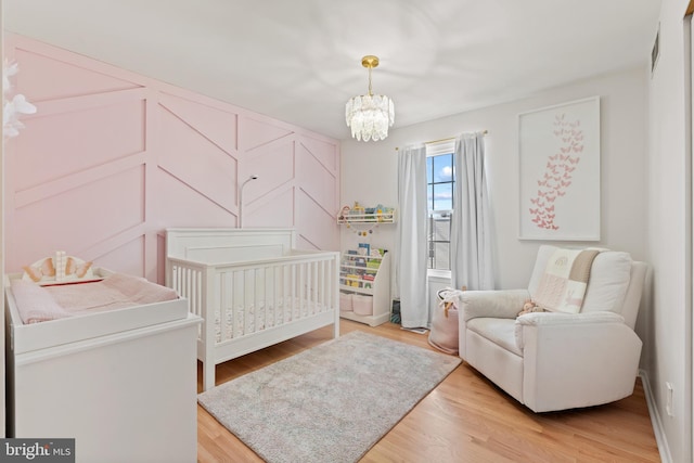 bedroom with a chandelier, a crib, light wood-type flooring, and a decorative wall