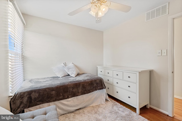 bedroom featuring a ceiling fan, visible vents, baseboards, and wood finished floors