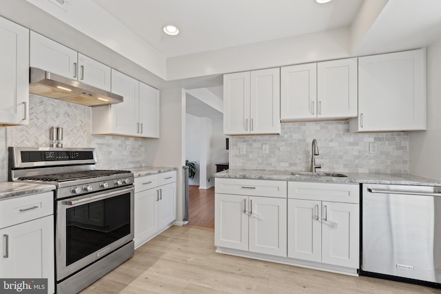 kitchen with under cabinet range hood, stainless steel appliances, a sink, white cabinets, and light wood finished floors