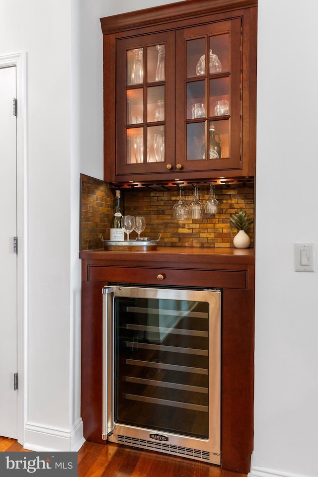 bar featuring a bar, wine cooler, wood finished floors, and tasteful backsplash