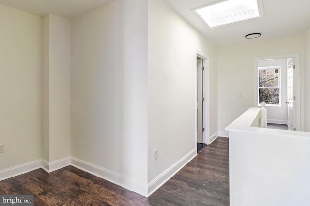 corridor with dark wood-type flooring, a skylight, and baseboards