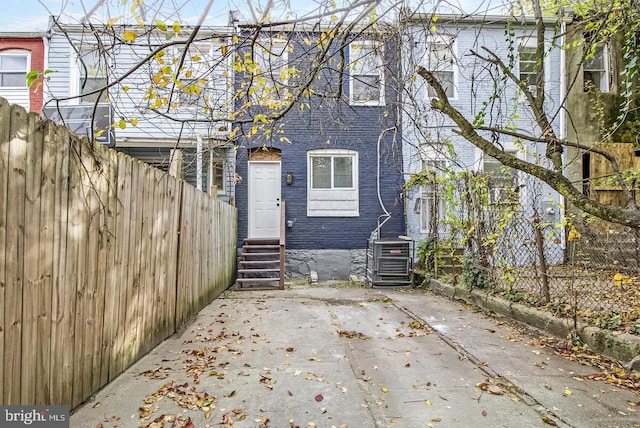 rear view of property with entry steps, a fenced backyard, central AC, brick siding, and a patio area