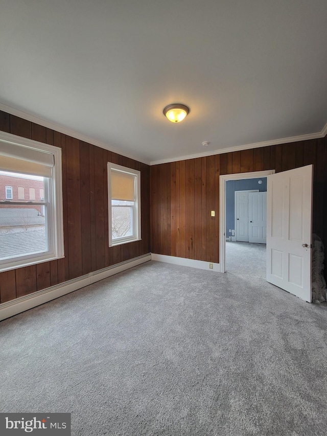 carpeted spare room with a baseboard heating unit, wood walls, baseboards, and crown molding