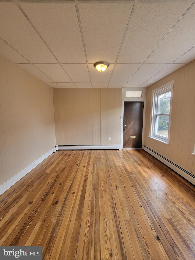 interior space featuring a baseboard heating unit, a drop ceiling, light wood-style flooring, and baseboards