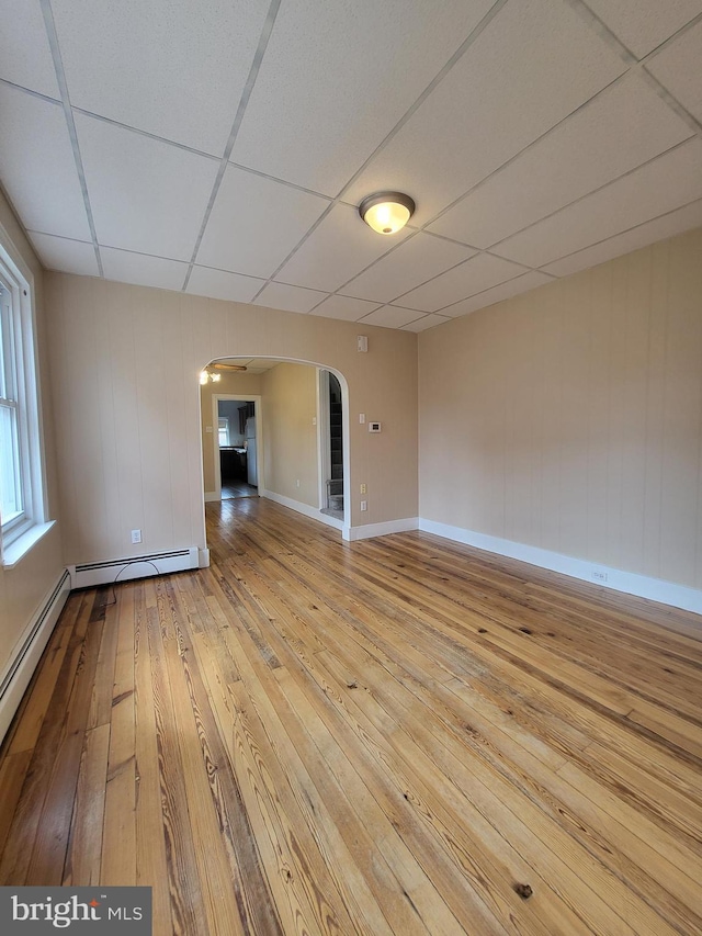 spare room featuring baseboards, arched walkways, a drop ceiling, hardwood / wood-style floors, and baseboard heating