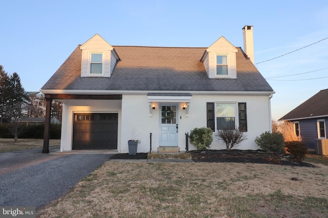 cape cod home featuring a shingled roof, a chimney, aphalt driveway, an attached garage, and a front lawn