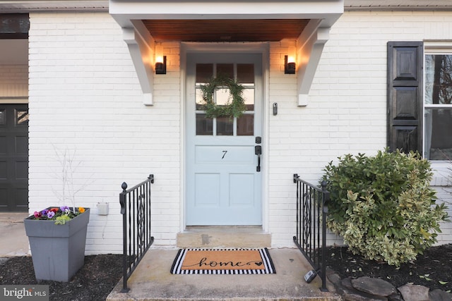 entrance to property featuring a garage and brick siding