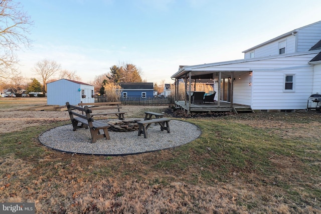 view of yard featuring an outdoor fire pit, fence, a deck, and an outdoor structure