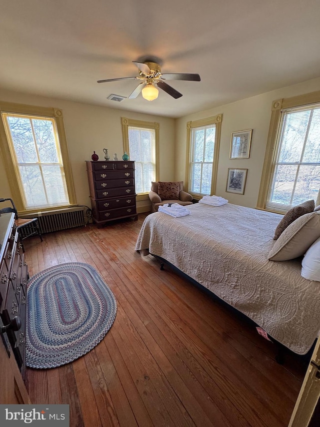 bedroom featuring radiator, wood-type flooring, visible vents, and multiple windows