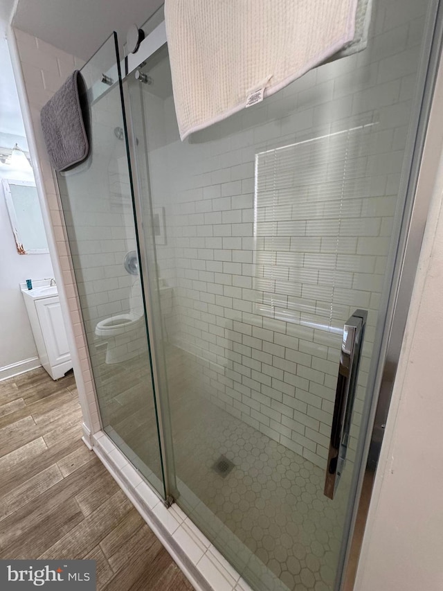 bathroom featuring wood tiled floor, vanity, baseboards, and a shower stall