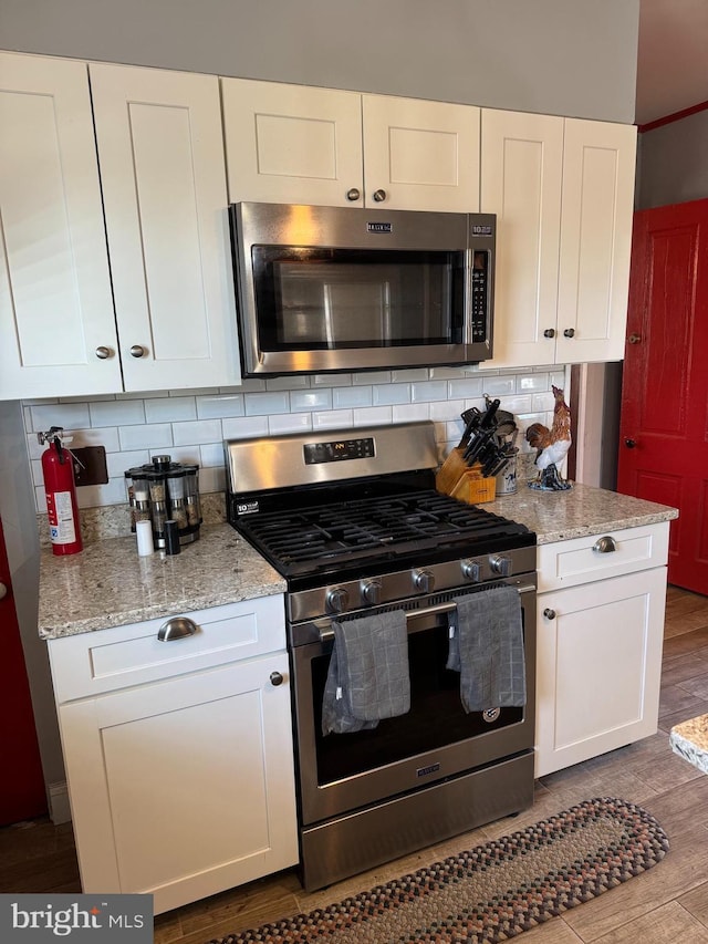 kitchen featuring stainless steel appliances, white cabinets, decorative backsplash, light stone countertops, and dark wood finished floors