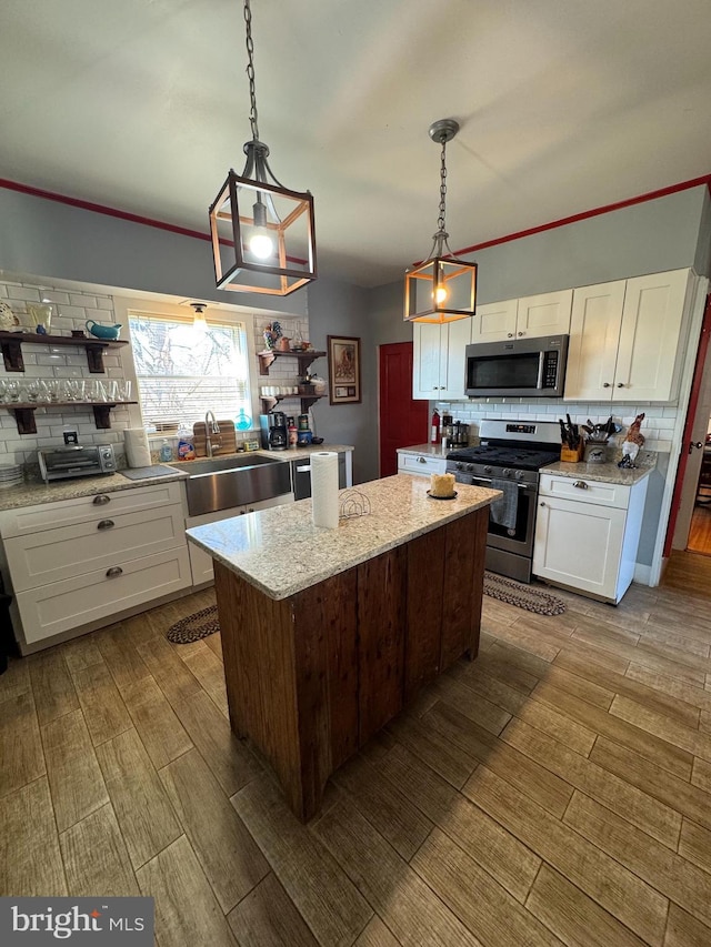 kitchen with stainless steel appliances, wood finish floors, a kitchen island, a sink, and white cabinetry