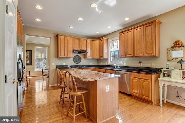 kitchen with a breakfast bar area, a sink, light wood-style floors, under cabinet range hood, and dishwasher