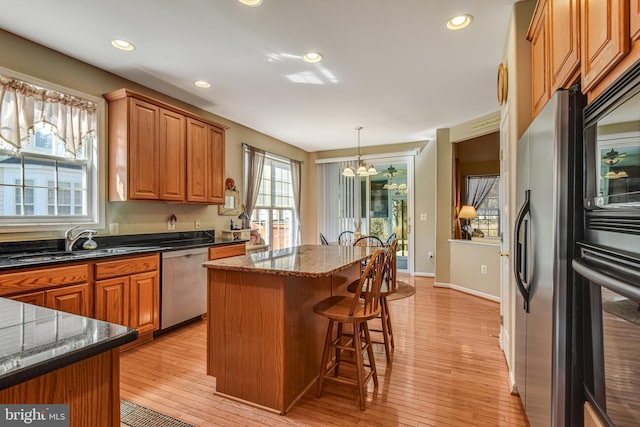 kitchen featuring a kitchen island, brown cabinets, a kitchen breakfast bar, stainless steel appliances, and a sink