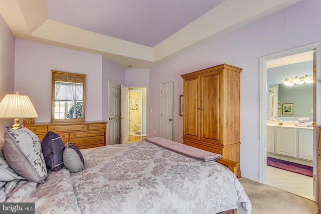 bedroom with connected bathroom, light colored carpet, and a tray ceiling