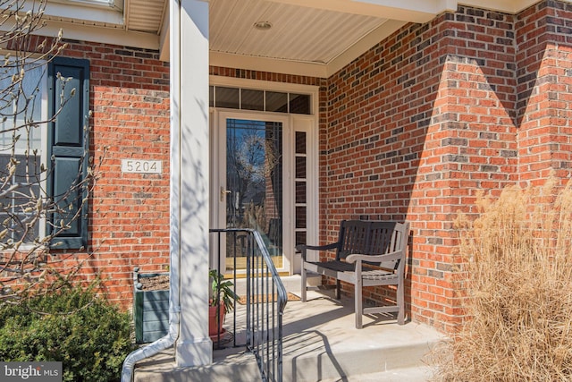 view of exterior entry with brick siding and covered porch