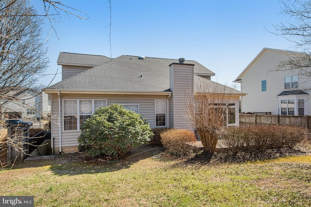 rear view of house with a yard, fence, a chimney, and a shingled roof