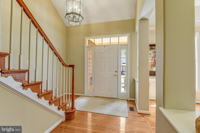 foyer featuring baseboards, stairs, a towering ceiling, a notable chandelier, and light wood-type flooring