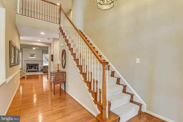 staircase featuring a fireplace with raised hearth, baseboards, recessed lighting, a high ceiling, and hardwood / wood-style flooring