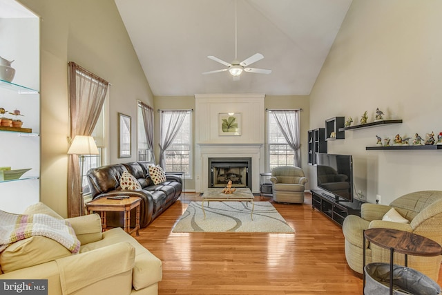 living area featuring ceiling fan, a large fireplace, high vaulted ceiling, and wood finished floors