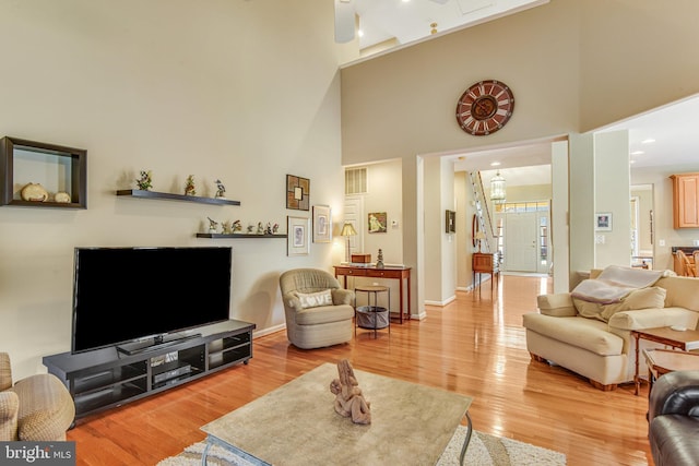 living room featuring visible vents, baseboards, a high ceiling, and light wood finished floors