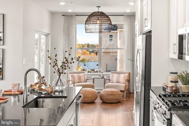 kitchen with dark countertops, appliances with stainless steel finishes, white cabinets, a sink, and wood finished floors