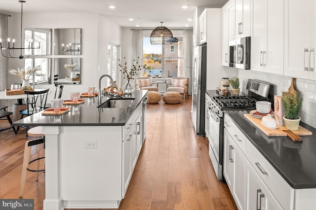 kitchen with a center island with sink, dark countertops, appliances with stainless steel finishes, light wood-type flooring, and a sink