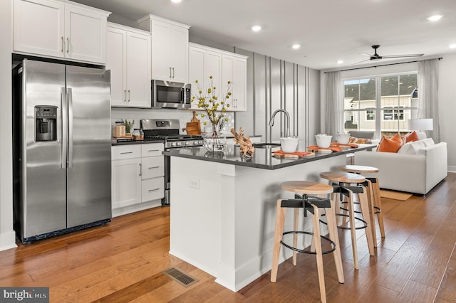 kitchen featuring a breakfast bar area, light wood-style floors, appliances with stainless steel finishes, an island with sink, and dark countertops