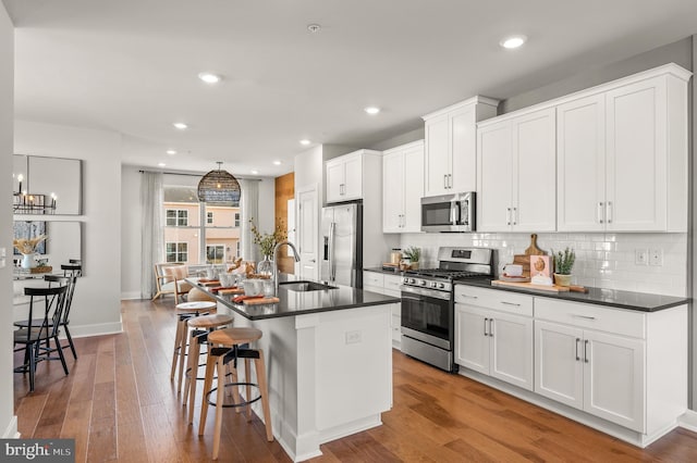 kitchen featuring dark countertops, decorative backsplash, appliances with stainless steel finishes, a sink, and hardwood / wood-style flooring