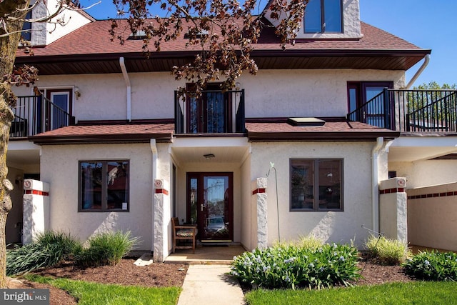 property entrance with roof with shingles, a balcony, and stucco siding