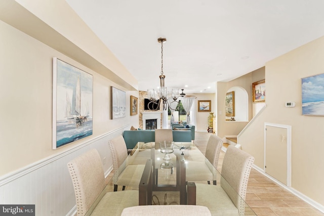 dining area with arched walkways, a wainscoted wall, light wood-type flooring, a fireplace, and a chandelier