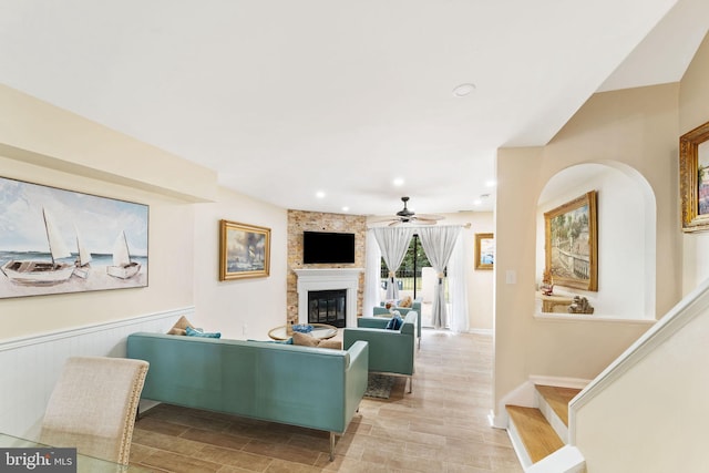 living area with stairway, a large fireplace, wainscoting, ceiling fan, and wood finished floors