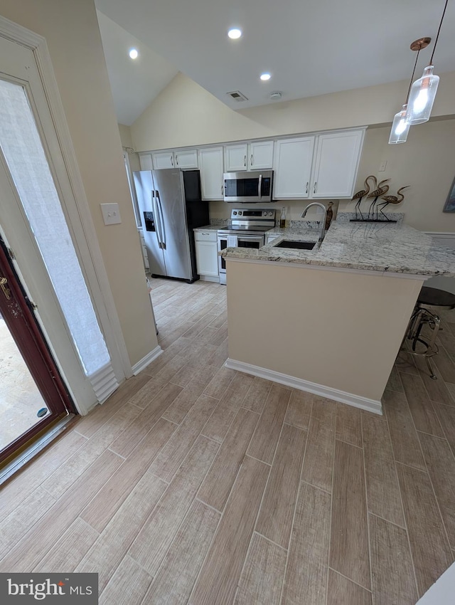 kitchen with light stone counters, stainless steel appliances, white cabinets, a sink, and a peninsula