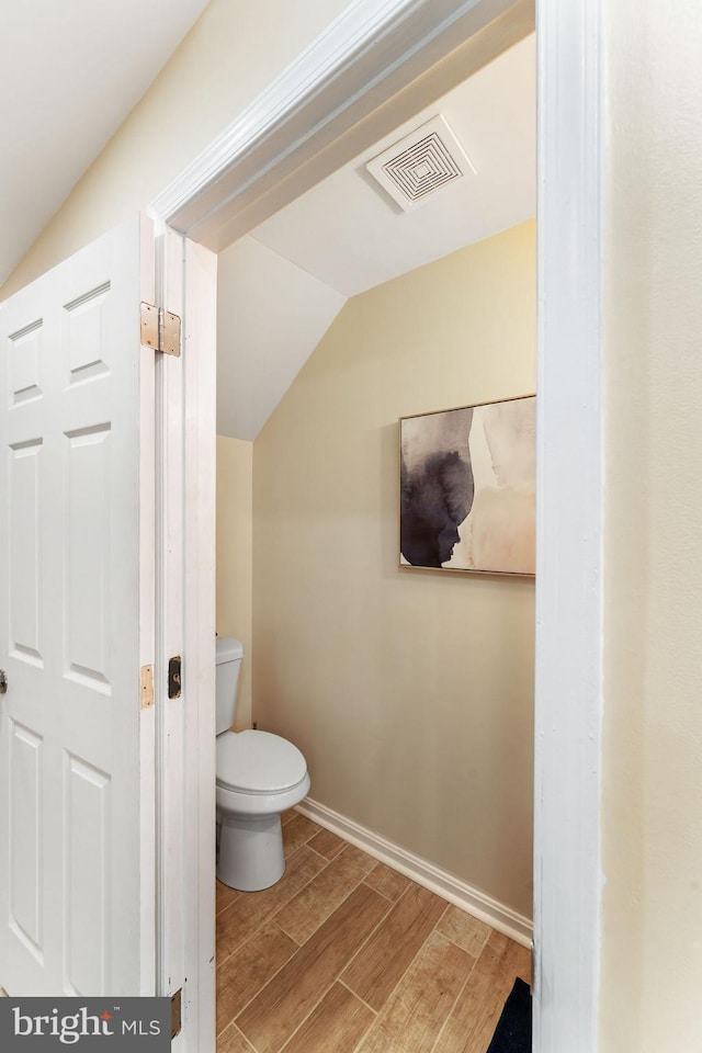 bathroom with toilet, wood finished floors, visible vents, baseboards, and vaulted ceiling