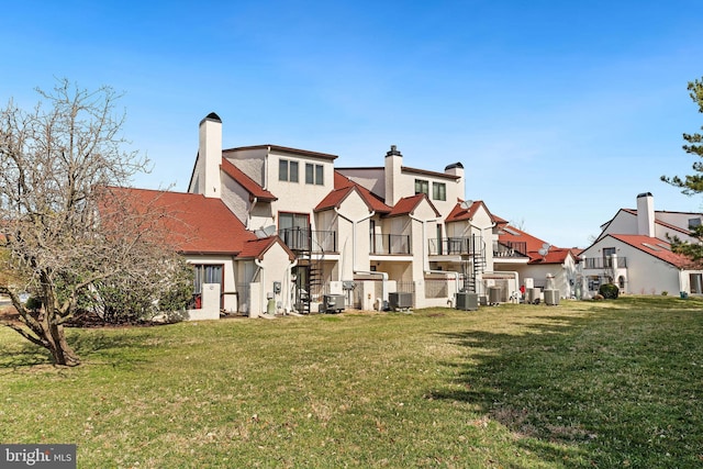 rear view of house with central air condition unit, a lawn, a residential view, and stucco siding