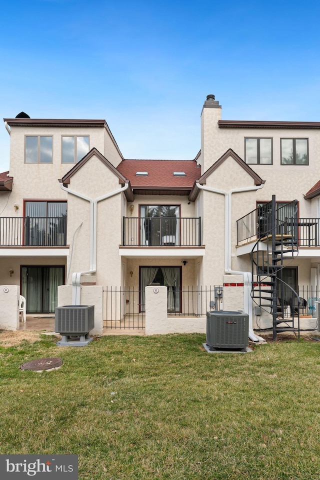 rear view of house featuring central air condition unit, fence private yard, a lawn, and stucco siding