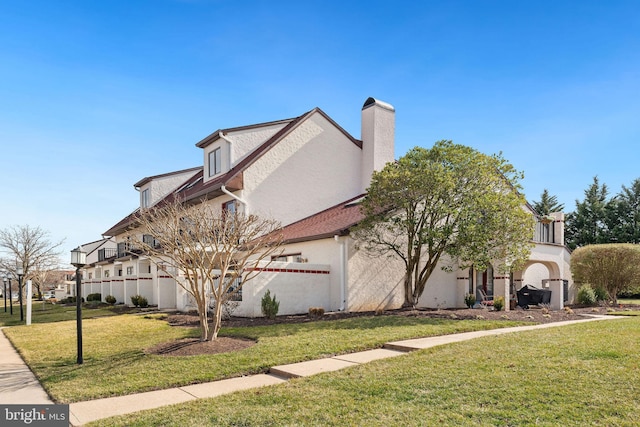 view of front of house featuring a front yard, a chimney, and stucco siding